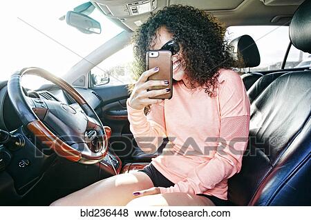 Stock Photo - Smiling Hispanic woman in car posing for cell phone selfie. Fotosearch