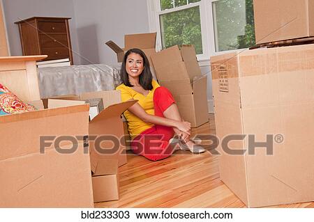 Stock Image - Smiling Hispanic woman sitting on floor with moving boxes. Fotosearch