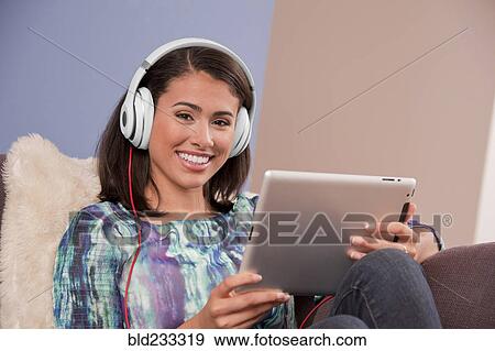 Smiling Hispanic woman sitting on sofa with digital tablet View Large Photo Image Stock Photo - Smiling Hispanic woman sitting on sofa with digital tablet. Fotosearch