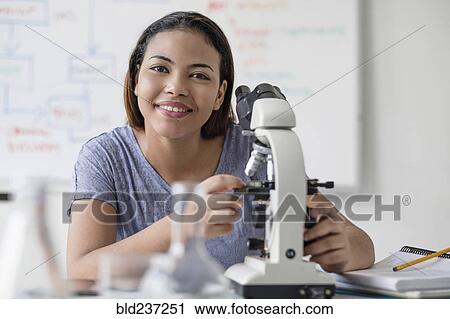 Stock Image - Smiling Hispanic woman using microscope. Fotosearch