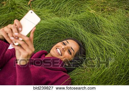 Smiling Indian woman laying in grass texting on cell phone View Large Photo Image Stock Photo - Smiling Indian woman laying in grass texting on cell phone. Fotosearch