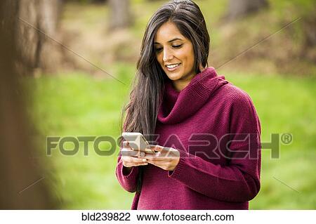Stock Image - Smiling Indian woman texting on cell phone. Fotosearch