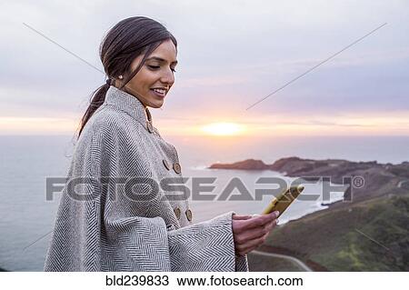 Smiling Indian woman texting on cell phone near shore View Large Photo Image Stock Image - Smiling Indian woman texting on cell phone near shore. Fotosearch
