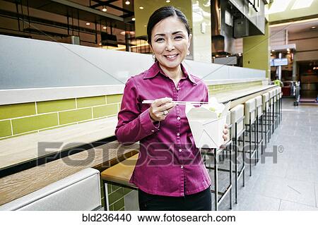 Stock Image - Smiling Japanese businesswoman posing in food court. Fotosearch