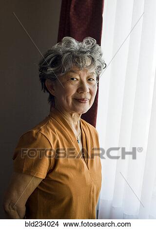 Picture - Smiling Japanese woman standing at window. Fotosearch