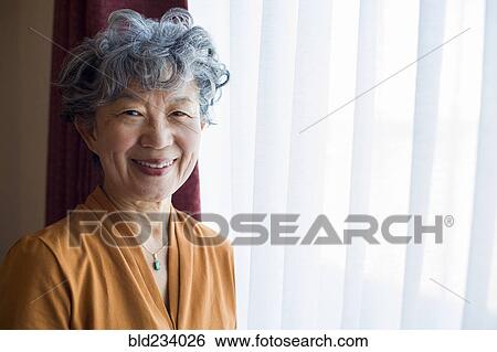 Stock Photograph - Smiling Japanese woman standing at window. Fotosearch