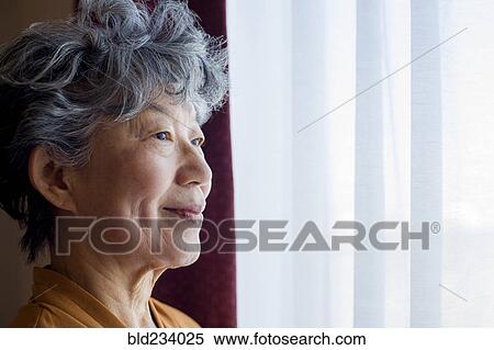 Stock Photography - Smiling Japanese woman standing at window. Fotosearch
