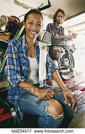 Stock Photo - Smiling man and woman repairing motorcycle in garage. Fotosearch