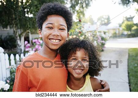 Picture - Smiling Mixed Race brother and sister hugging outdoors. Fotosearch
