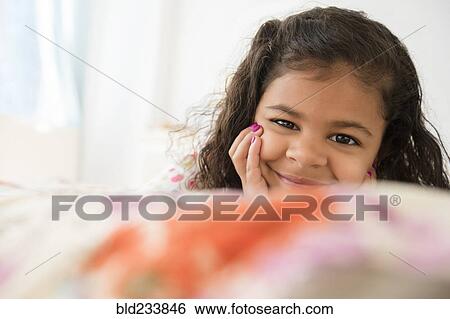 Smiling Mixed Race girl laying on bed View Large Photo Image Stock Photograph - Smiling Mixed Race girl laying on bed. Fotosearch