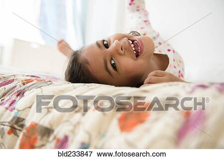 Stock Photo - Smiling Mixed Race girl rolling on bed. Fotosearch