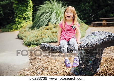 Stock Photography - Smiling Mixed Race girl sitting on stone bench in park. Fotosearch
