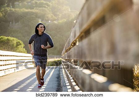 Stock Photo - Smiling Mixed Race man running on footbridge. Fotosearch