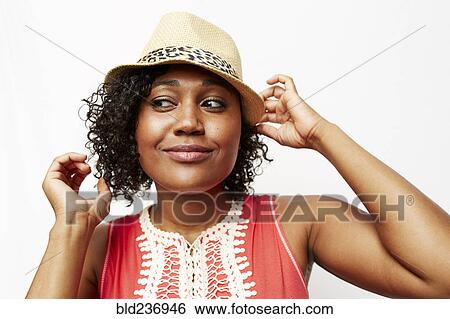 Stock Photograph - Smiling Mixed Race woman adjusting hat. Fotosearch