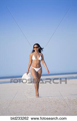 Stock Image - Smiling Mixed Race woman carrying sun hat on beach. Fotosearch