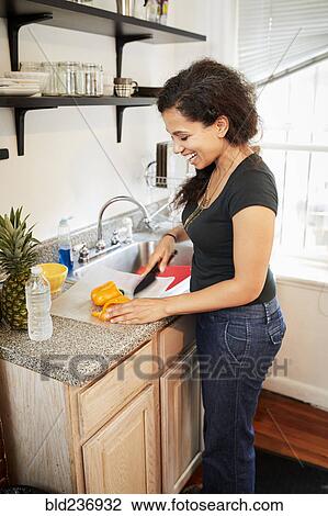 Stock Image - Smiling Mixed Race woman chopping pepper on cutting board. Fotosearch