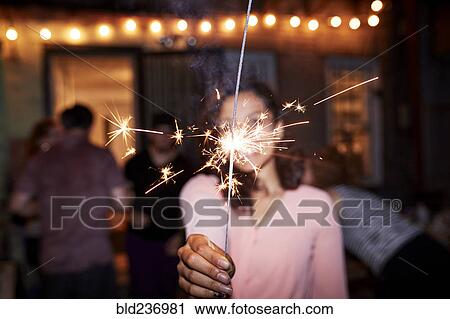 Smiling Mixed Race woman holding burning sparkler at backyard party View Large Photo Image Stock Image - Smiling Mixed Race woman holding burning sparkler at backyard party. Fotosearch