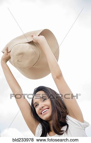 Stock Photo - Smiling Mixed Race woman holding sun hat. Fotosearch