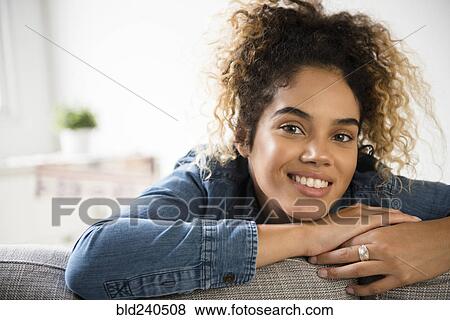 Stock Photo - Smiling Mixed Race woman leaning on sofa. Fotosearch
