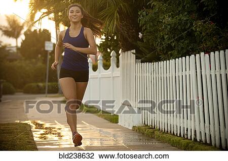 Stock Image - Smiling Mixed Race woman running on sidewalk. Fotosearch