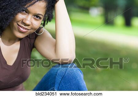 Stock Image - Smiling Mixed Race woman sitting in park. Fotosearch