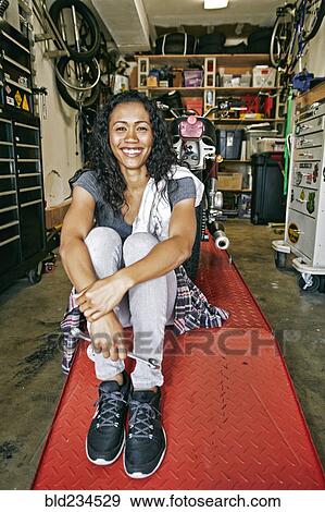 Smiling Mixed Race woman sitting on repair stand in garage View Large Photo Image Stock Photo - Smiling Mixed Race woman sitting on repair stand in garage. Fotosearch
