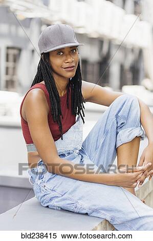Stock Photography - Smiling Mixed Race woman sitting on wall. Fotosearch