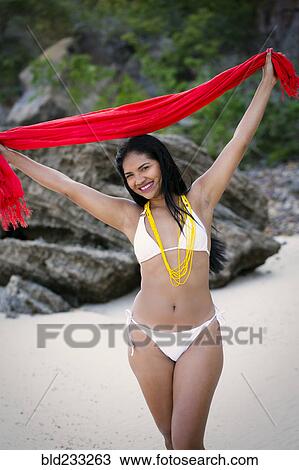 Stock Image - Smiling Mixed Race woman wearing bikini holding red scarf. Fotosearch