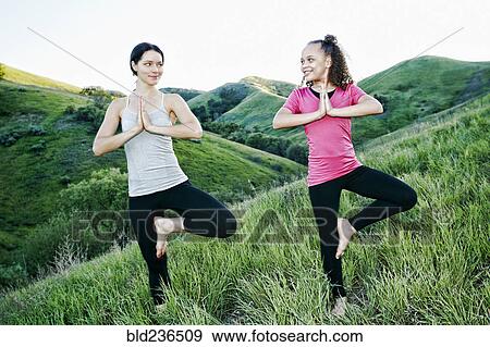 Stock Photo - Smiling mother and daughter practicing yoga on hill. Fotosearch