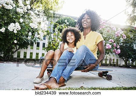 Stock Photo - Smiling mother and daughter sitting on skateboard. Fotosearch
