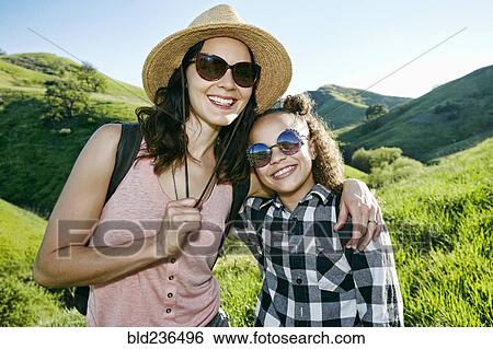 Stock Photograph - Smiling mother and daughter wearing sunglasses on hill. Fotosearch