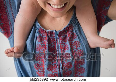 Stock Image - Smiling mother carrying baby son on shoulders. Fotosearch