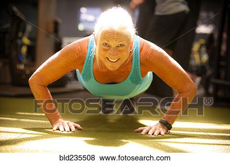 Stock Photo - Smiling older woman doing push-up on gymnasium floor. Fotosearch