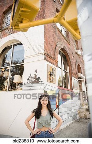 Stock Image - Smiling Thai woman posing on city sidewalk. Fotosearch
