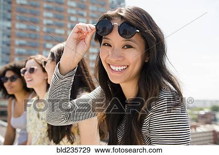 Stock Photo - Smiling woman lifting sunglasses outdoors. Fotosearch