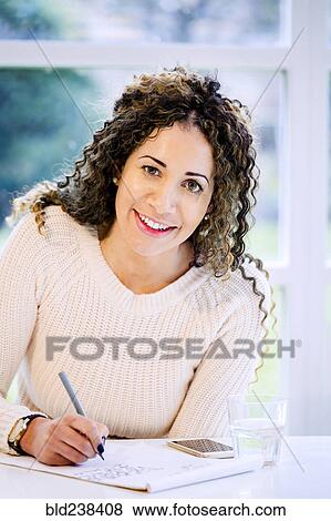 Smiling woman sitting at table writing on notepad with pen View Large Photo Image Stock Photo - Smiling woman sitting at table writing on notepad with pen. Fotosearch