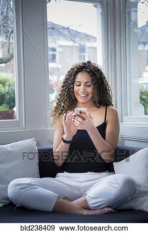 Smiling woman sitting near window texting on cell phone View Large Photo Image Stock Photo - Smiling woman sitting near window texting on cell phone. Fotosearch