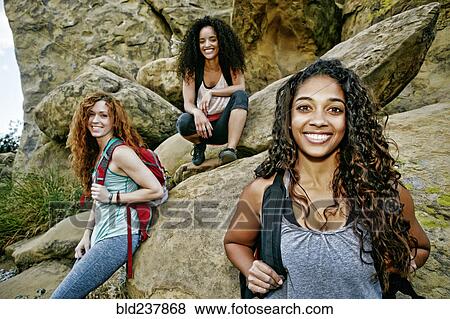Stock Photo - Smiling women carrying backpacks near rock formation. Fotosearch