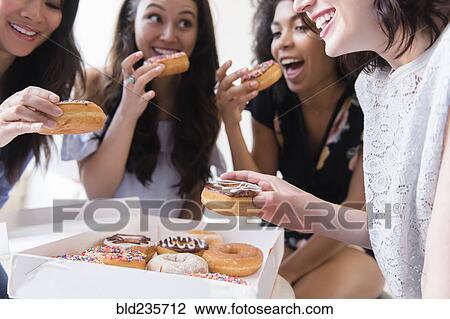 Stock Image - Smiling women eating donuts. Fotosearch