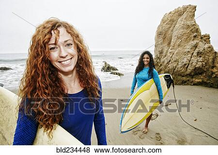 Stock Photo - Smiling women holding surfboards at beach. Fotosearch