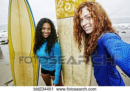 Smiling women holding surfboards posing for selfie at beach View Large Photo Image Stock Image - Smiling women holding surfboards posing for selfie at beach . Fotosearch