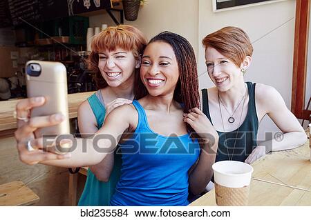 Smiling women posing for cell phone selfie in coffee shop View Large Photo Image Picture - Smiling women posing for cell phone selfie in coffee shop. Fotosearch