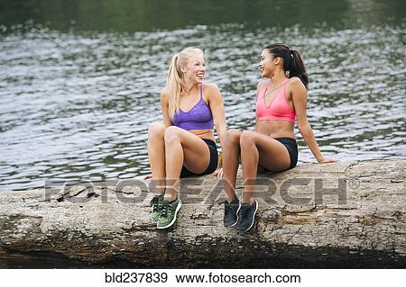 Smiling women sitting on log near lake View Large Photo Image Stock Photo - Smiling women sitting on log near lake. Fotosearch