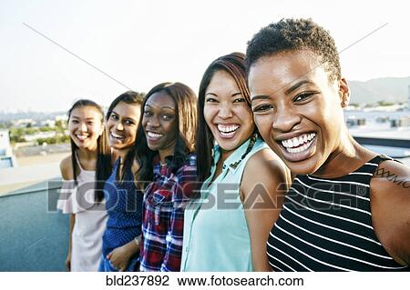 Stock Image - Smiling women standing in a row on rooftop. Fotosearch