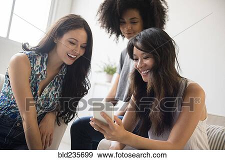 Stock Photo - Smiling women texting on cell phone in livingroom. Fotosearch
