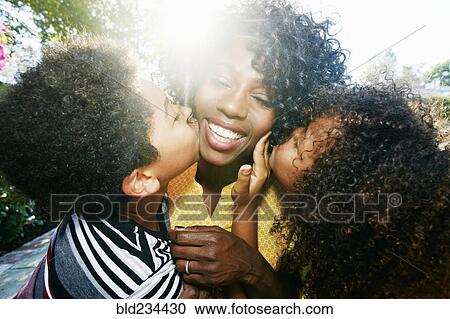 Stock Image - Son and daughter kissing cheeks of mother outdoors. Fotosearch
