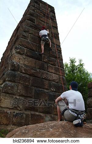 Picture - Spotter watching friend climbing urban brick wall. Fotosearch