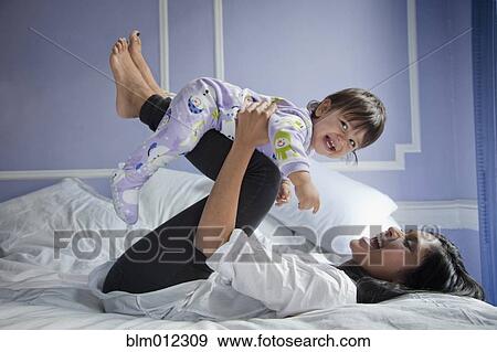Stock Photo - Sri Lankan mother playing with baby girl on bed. Fotosearch