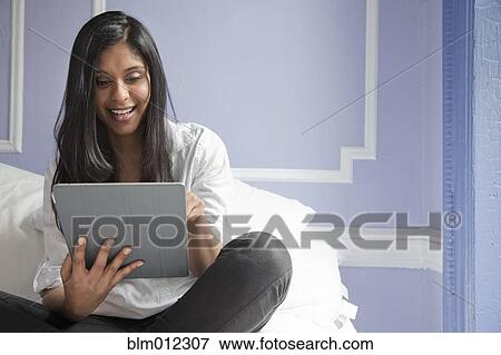 Stock Photo - Sri Lankan woman on bed using digital tablet. Fotosearch