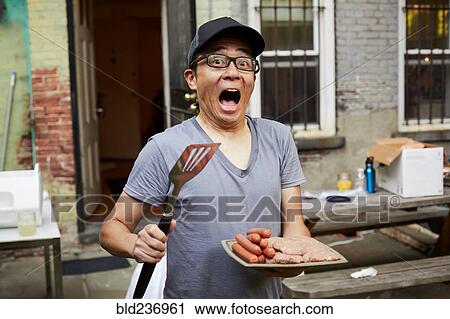 Stock Image - Surprised Japanese man holding plate of raw meat in backyard. Fotosearch